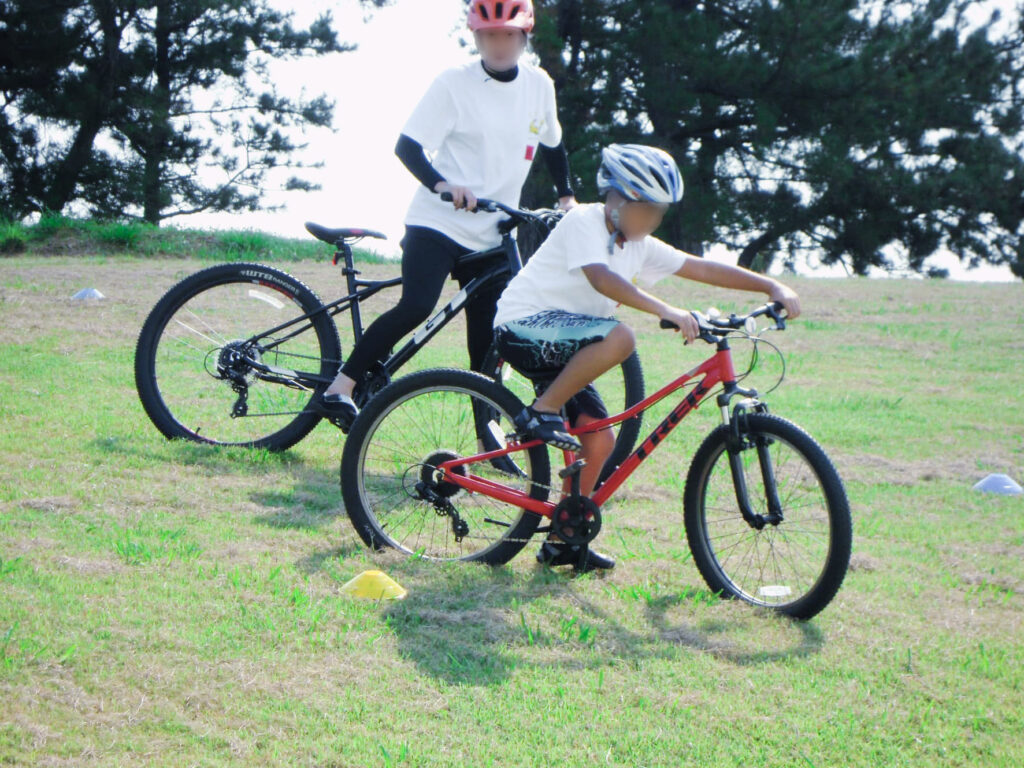 芝生の斜面でヘルメットをかぶって自転車の練習をする親子の様子