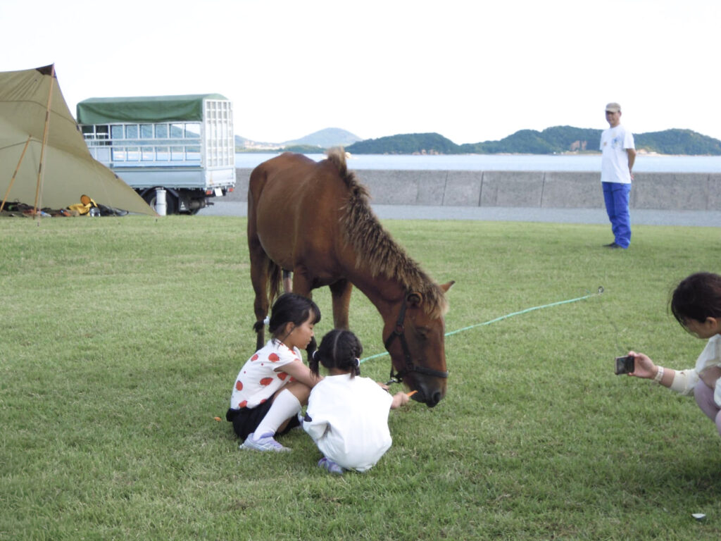 芝生の上で馬ににんじんをあげる子どもたち